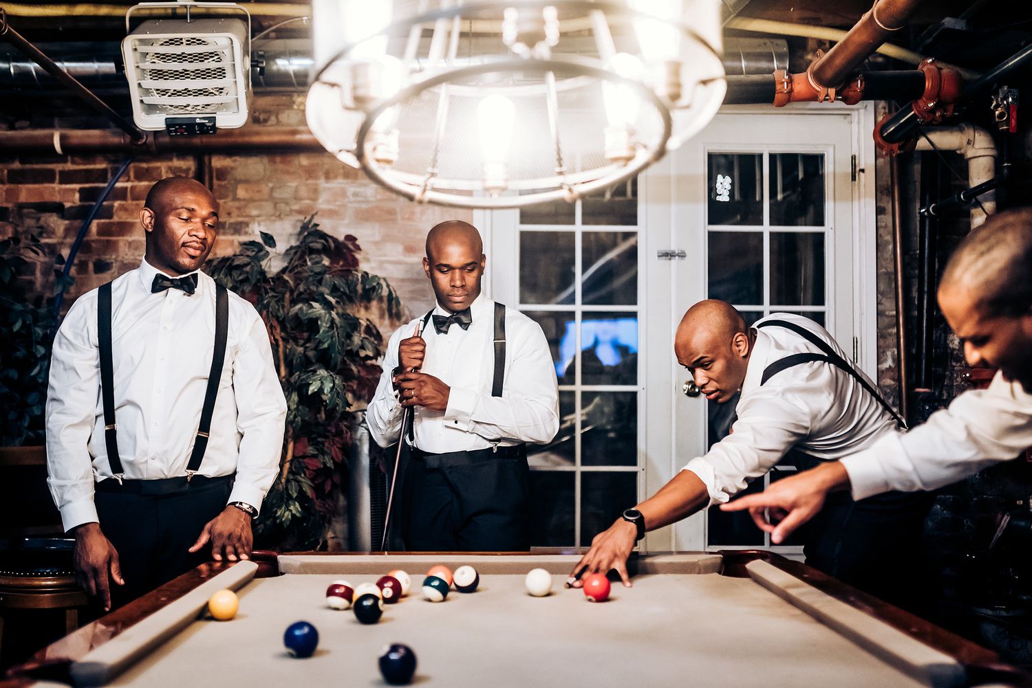 Groomsmen play pool at the wedding venue while wearing formal attire.