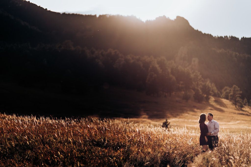 Couple standing in vast mountain meadow during golden hour.