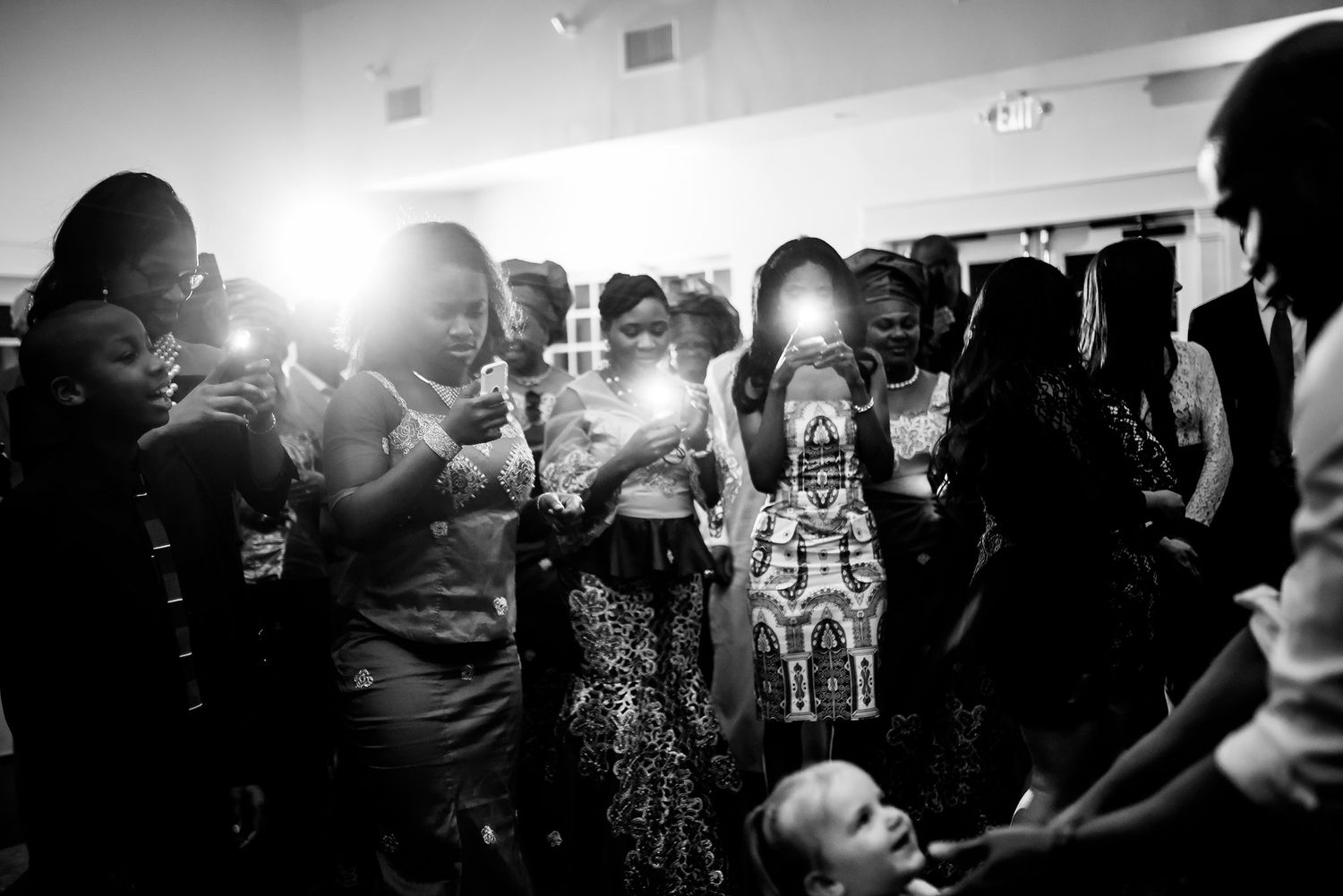Black and white photo of wedding reception guests dancing in dramatic lighting.