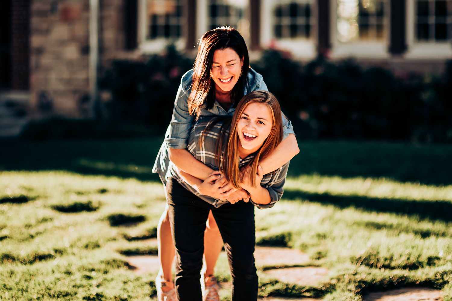 Two people share a playful moment while laughing together on a sunny lawn.