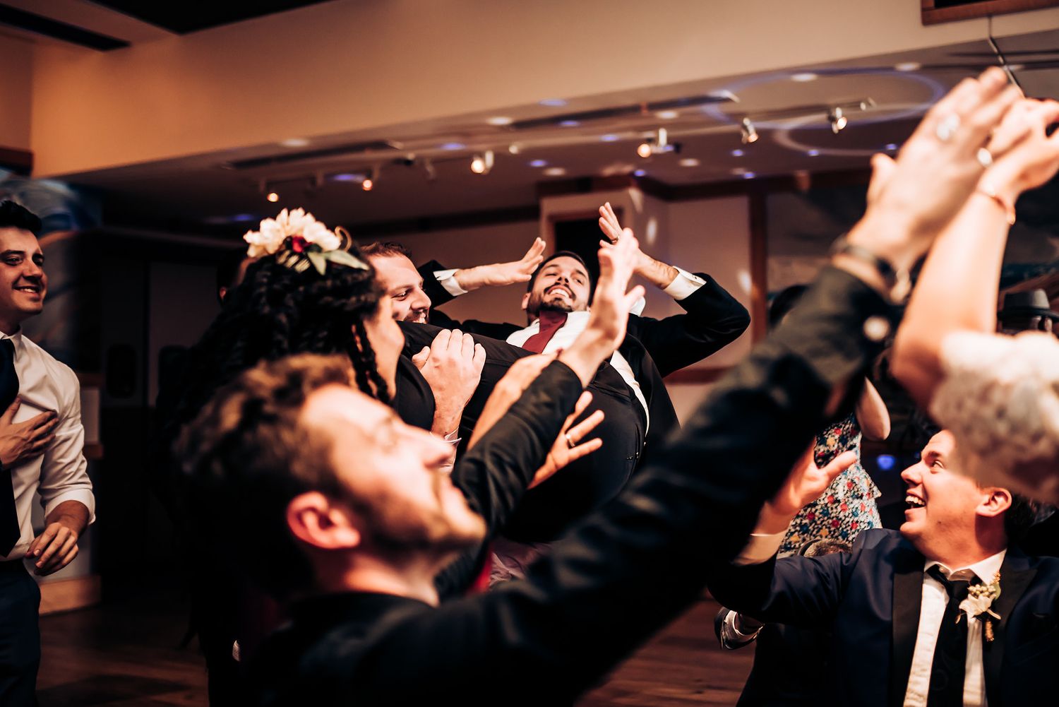 Party guests raise their hands in celebration during indoor event under dim lighting.