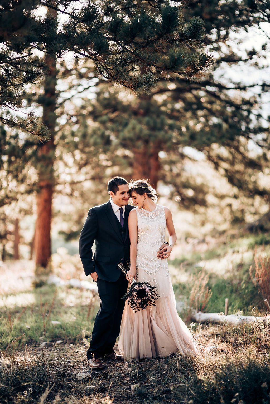 Elegant couple walking mountain trail in formal attire with pine forest backdrop.
