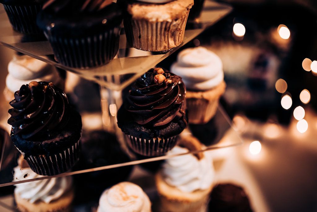 Artistically lit chocolate cupcakes with swirled frosting displayed at a wedding reception.