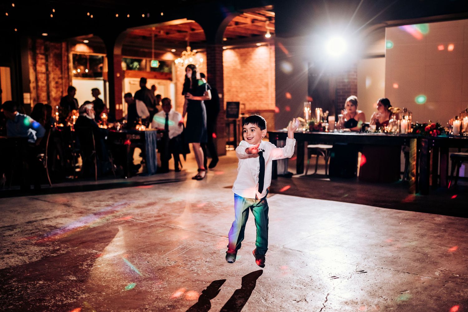 Dancing guests enjoy celebration on illuminated dance floor at wedding reception.