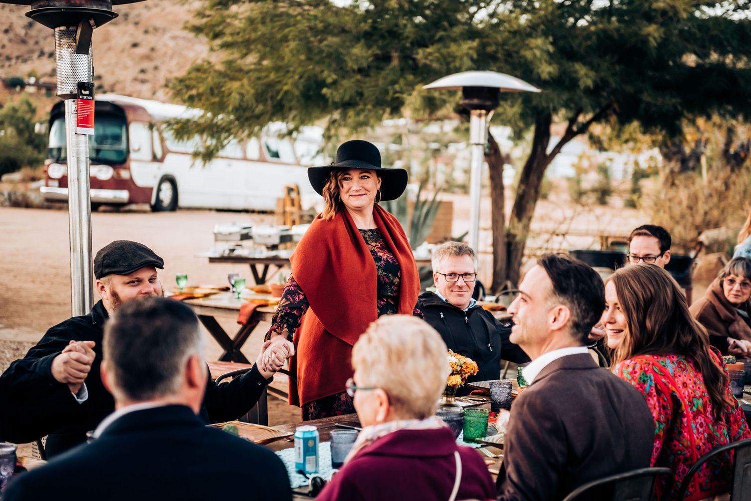 Outdoor dinner party gathering in desert setting with string lights and heater lamps.