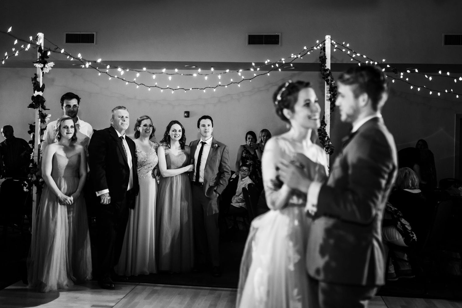 A black and white photo of a wedding couple dancing while guests watch in the background.