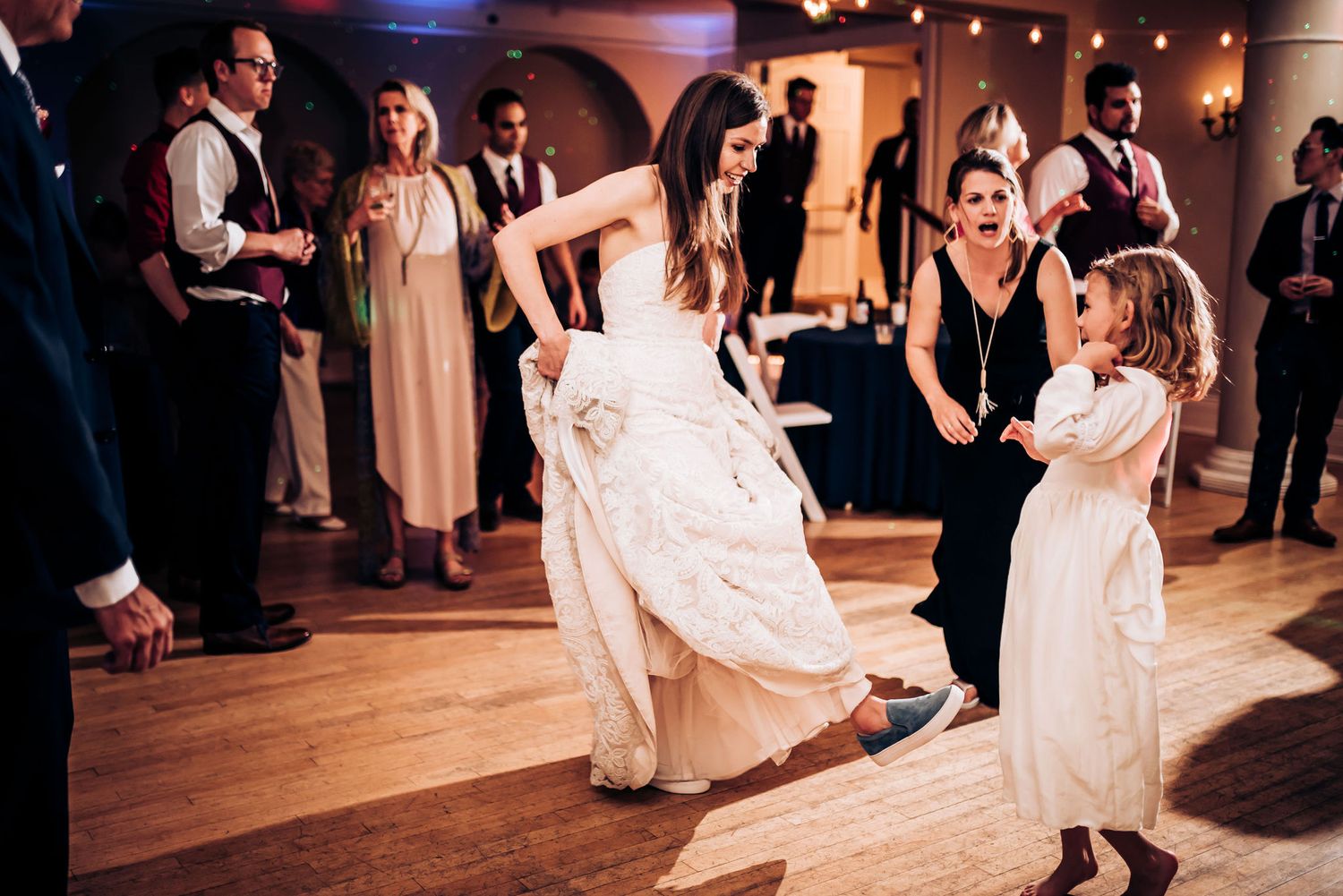 Wedding guests dancing on a wooden dance floor with a bride in a white dress.