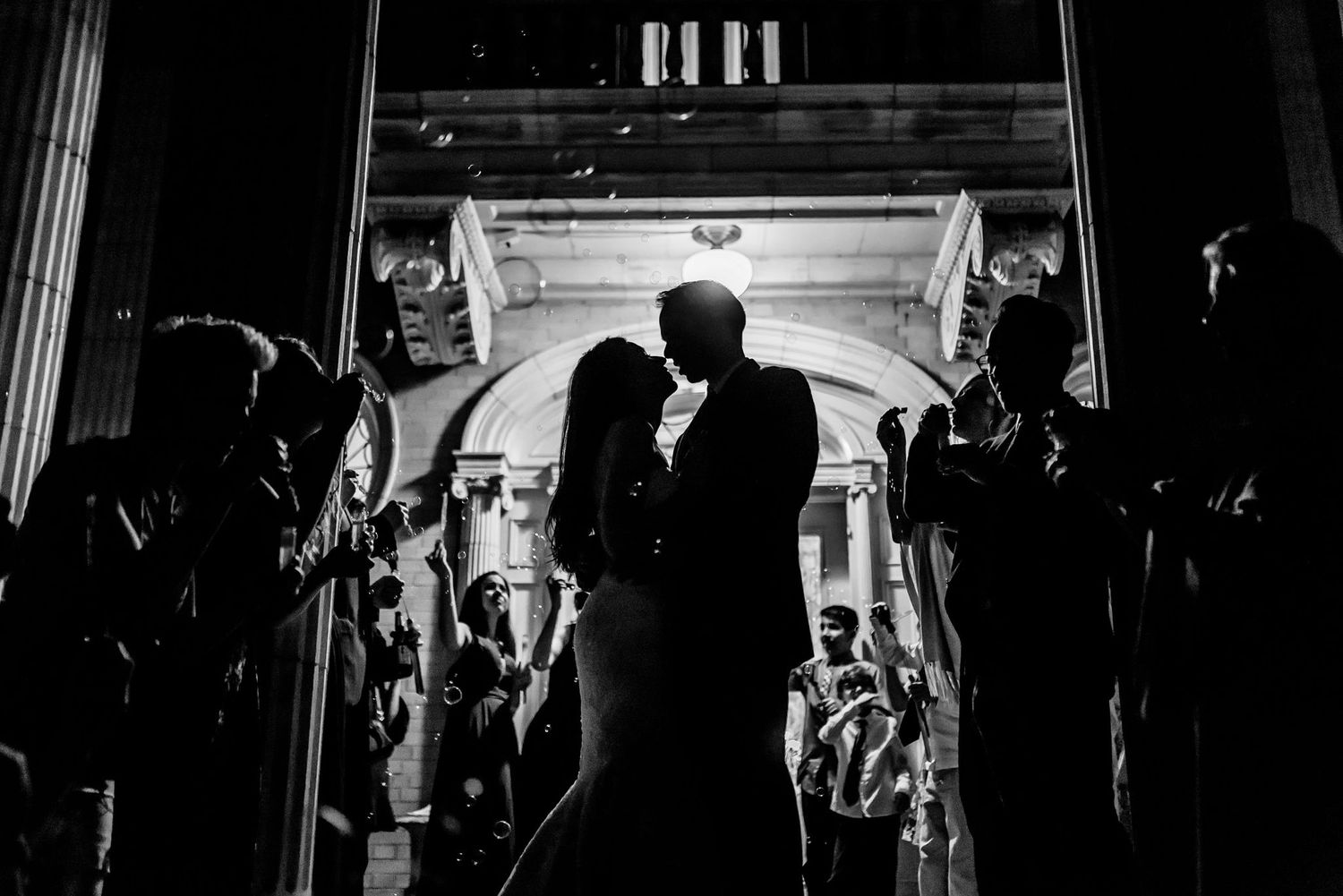 Silhouetted couple sharing intimate moment during sparkler exit under grand archway.