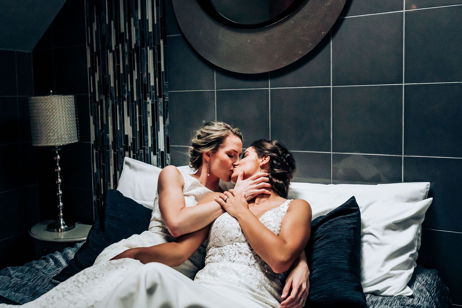 Intimate wedding moment captured in modern room with dark tiled walls and circular mirror.