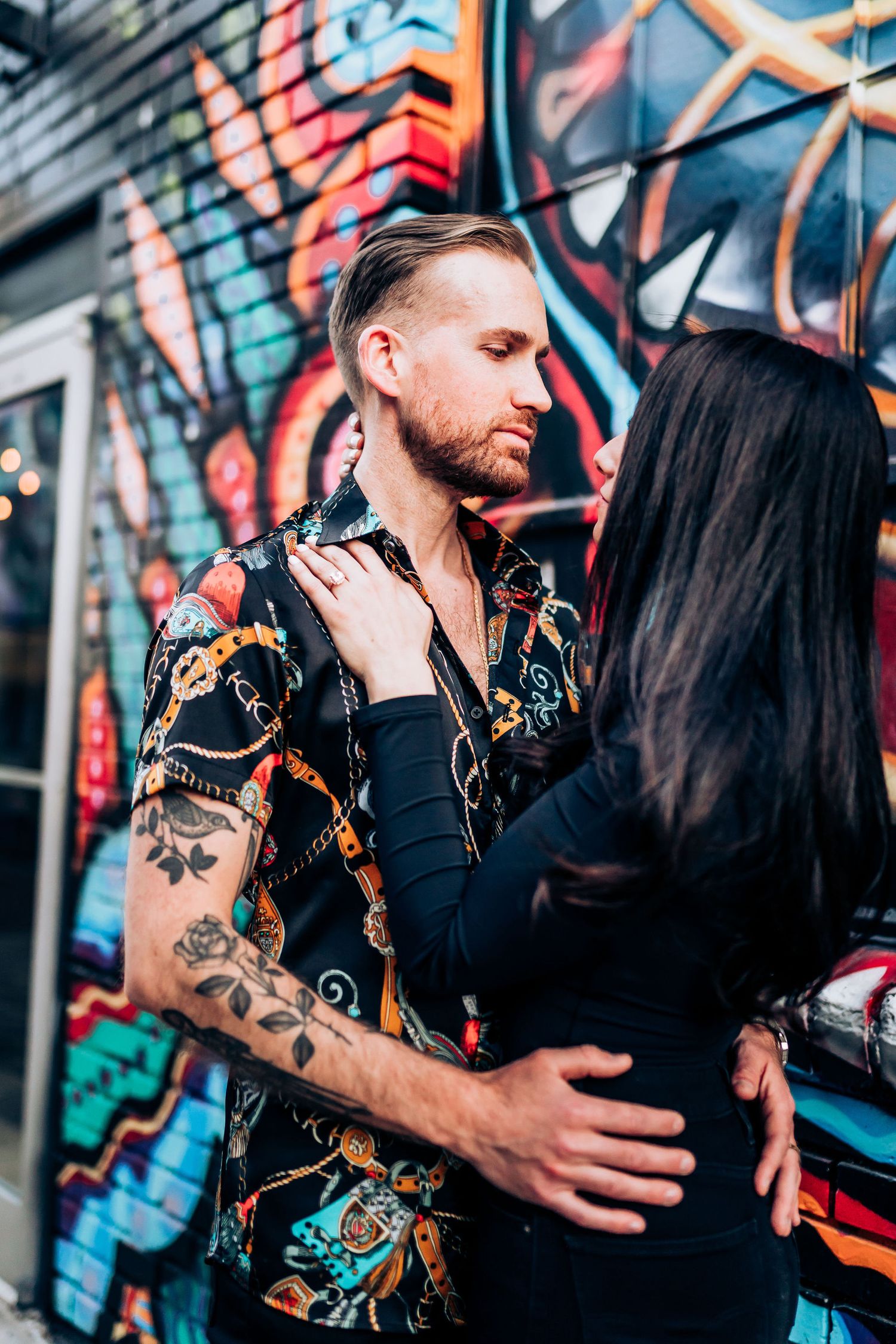 Intimate portrait against urban graffiti wall showing close embrace.