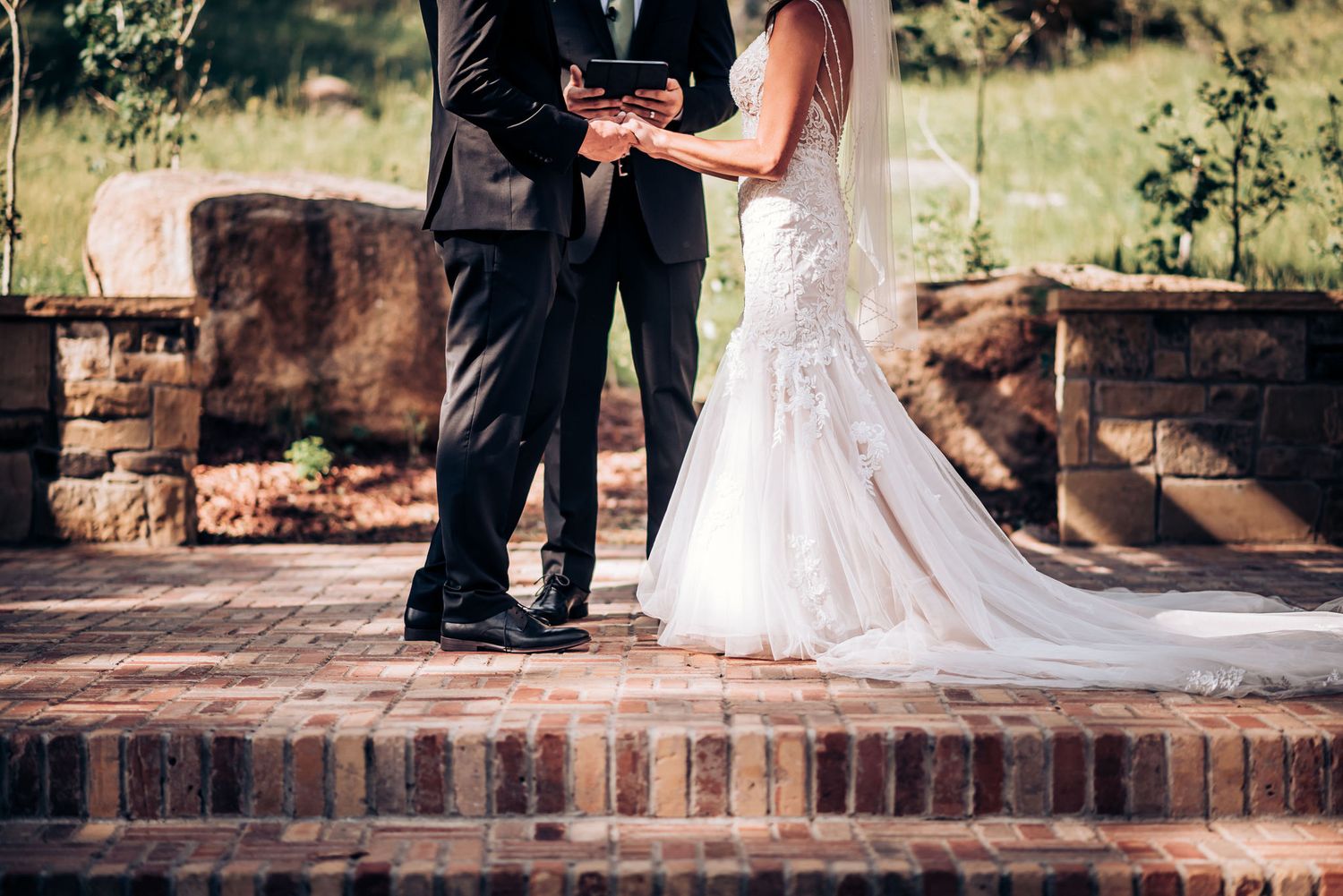Close-up of wedding couple exchanging vows on brick steps during outdoor ceremony.