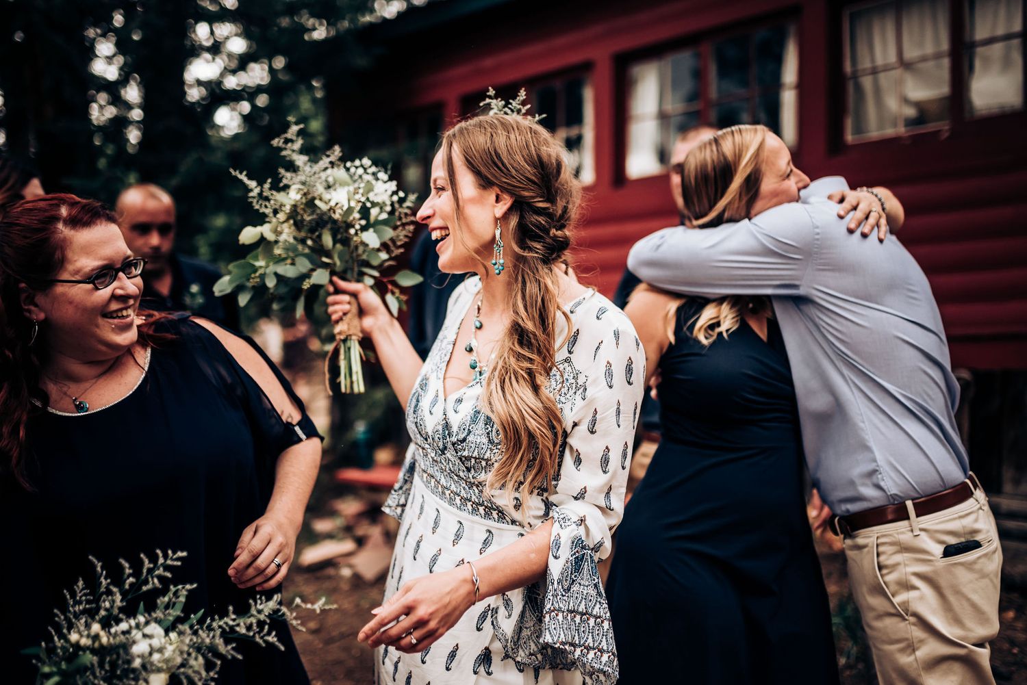 A candid moment of celebration with floral bouquets outside a red cabin.