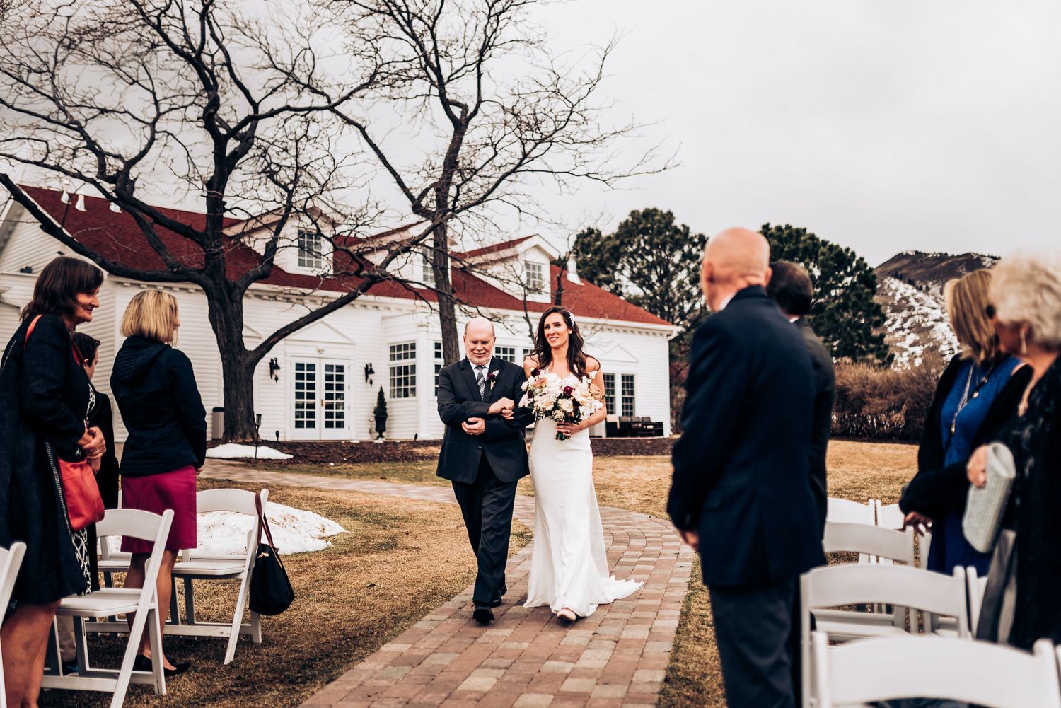 Wedding procession along brick pathway with white colonial building in background.