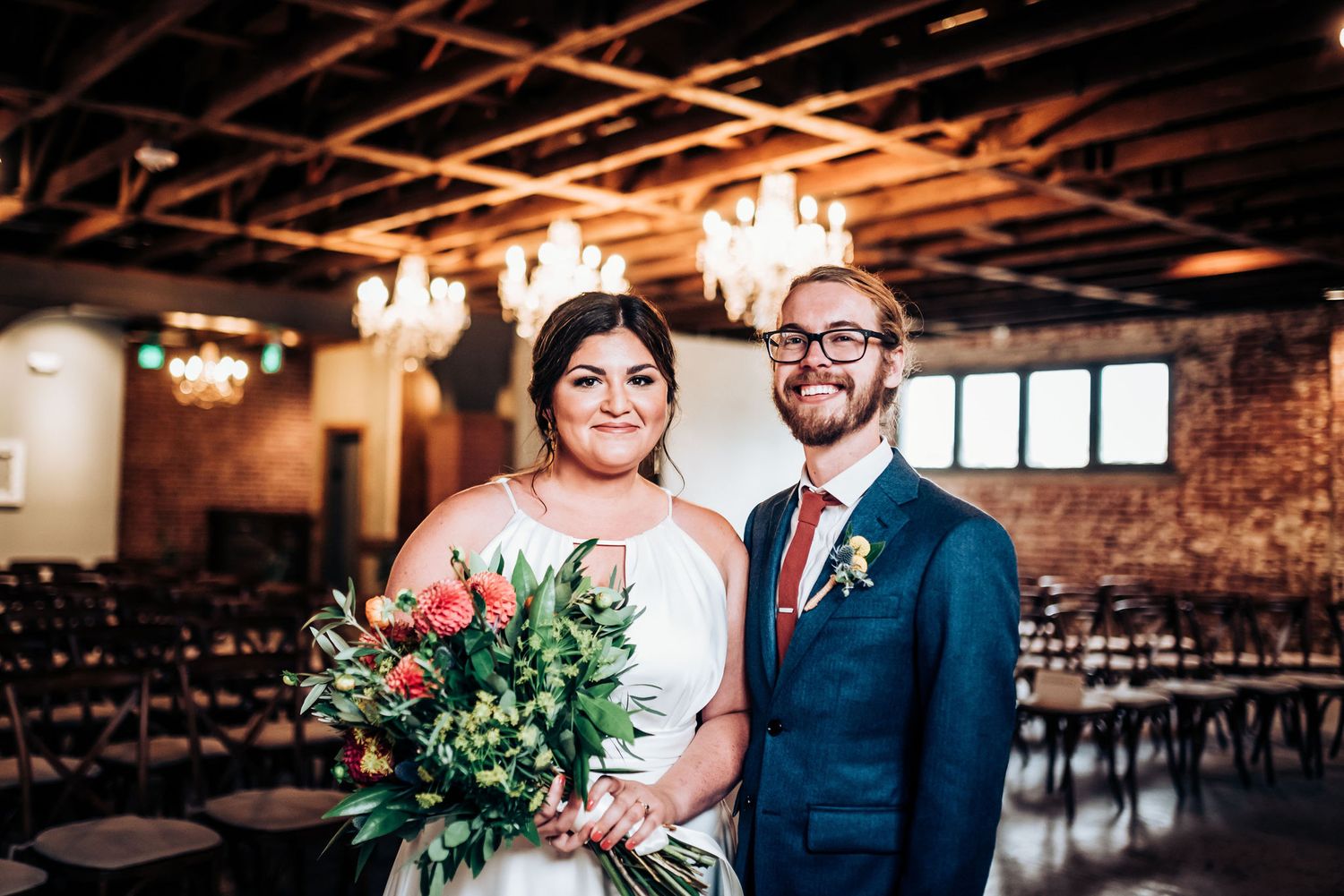 Wedding couple poses in industrial venue with exposed brick walls and elegant chandeliers.