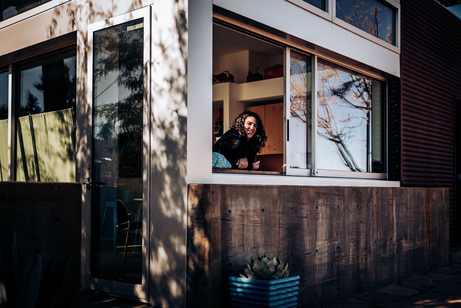 Figure visible through modern window frame of wooden building with dappled sunlight.
