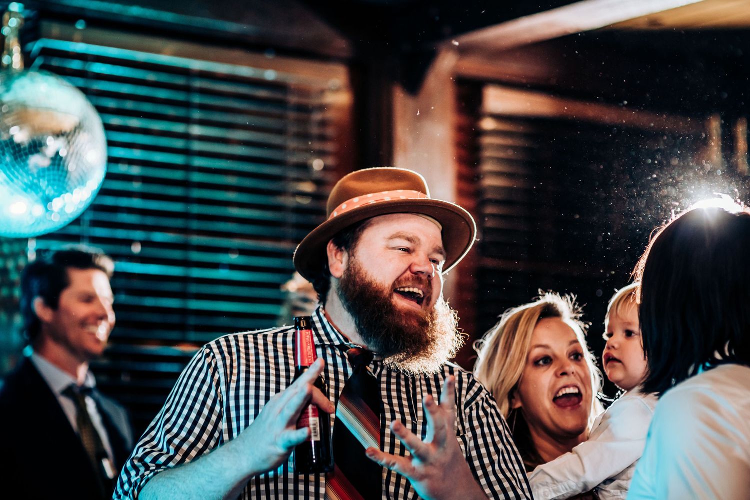 Enthusiastic partygoers celebrating with drinks under a disco ball at a lively indoor event.