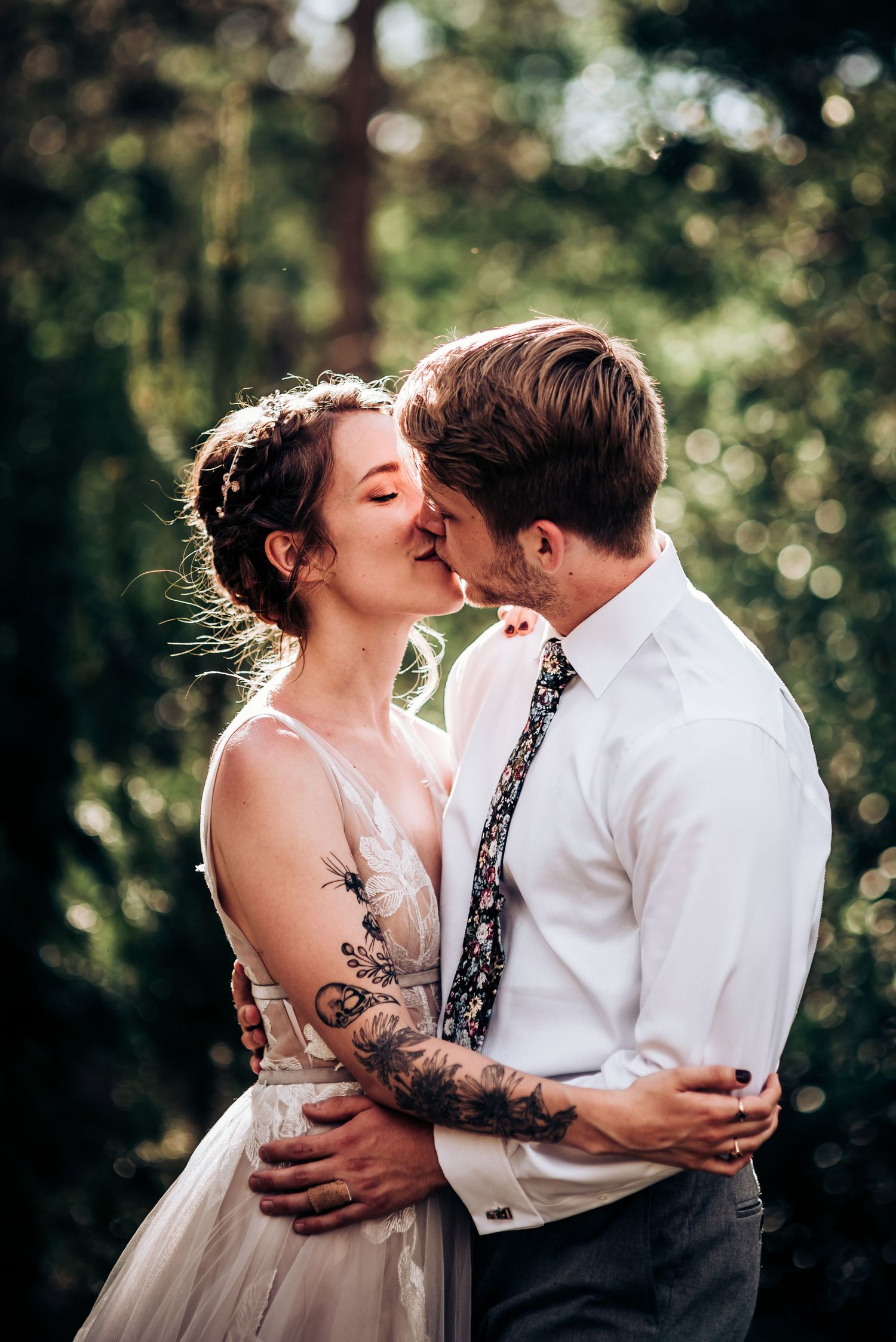 An intimate forest wedding kiss captured with soft bokeh lighting through the trees.