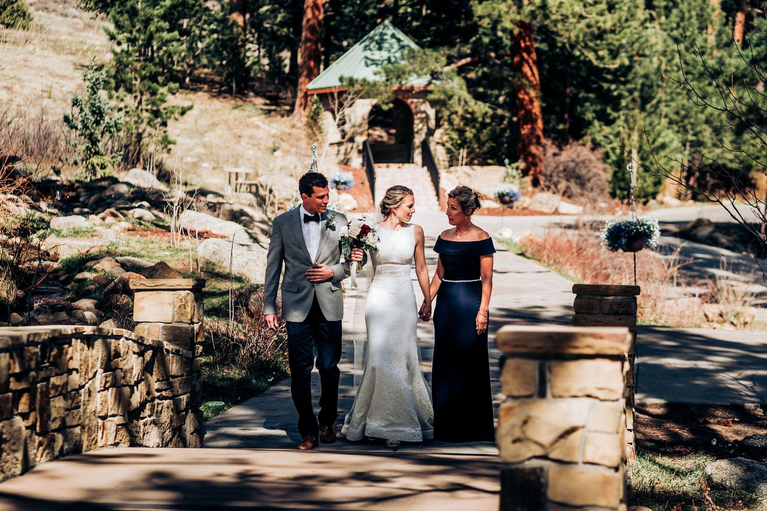 Wedding ceremony participants standing together on a stone pathway surrounded by evergreen trees.