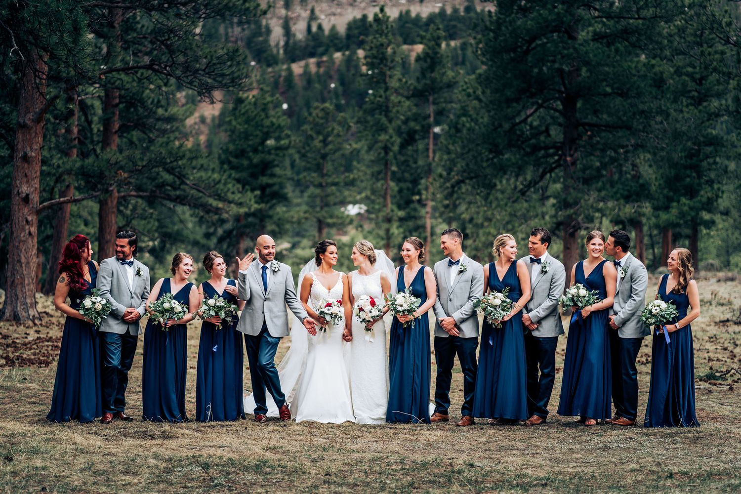 Wedding party in navy blue attire poses in mountain forest setting.