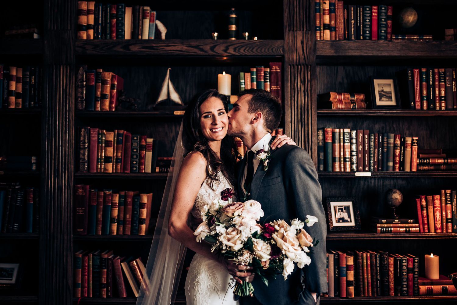 Romantic wedding portrait of couple embracing in front of vintage library bookshelves.