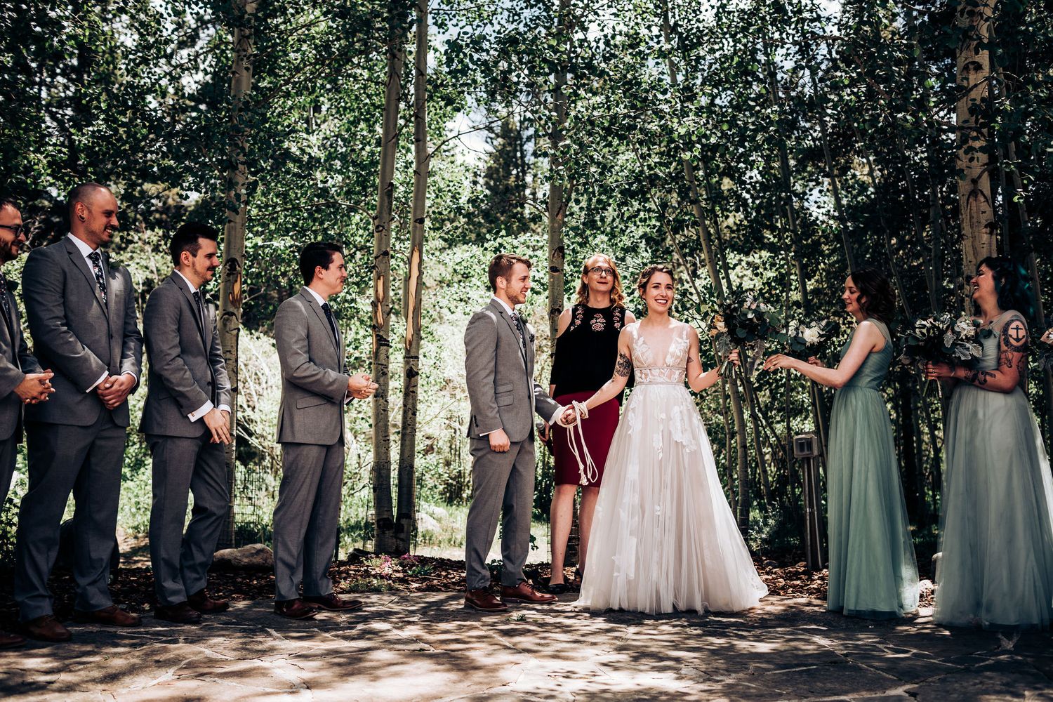 A wedding party lines up during an outdoor forest ceremony with bridesmaids in sage green dresses.