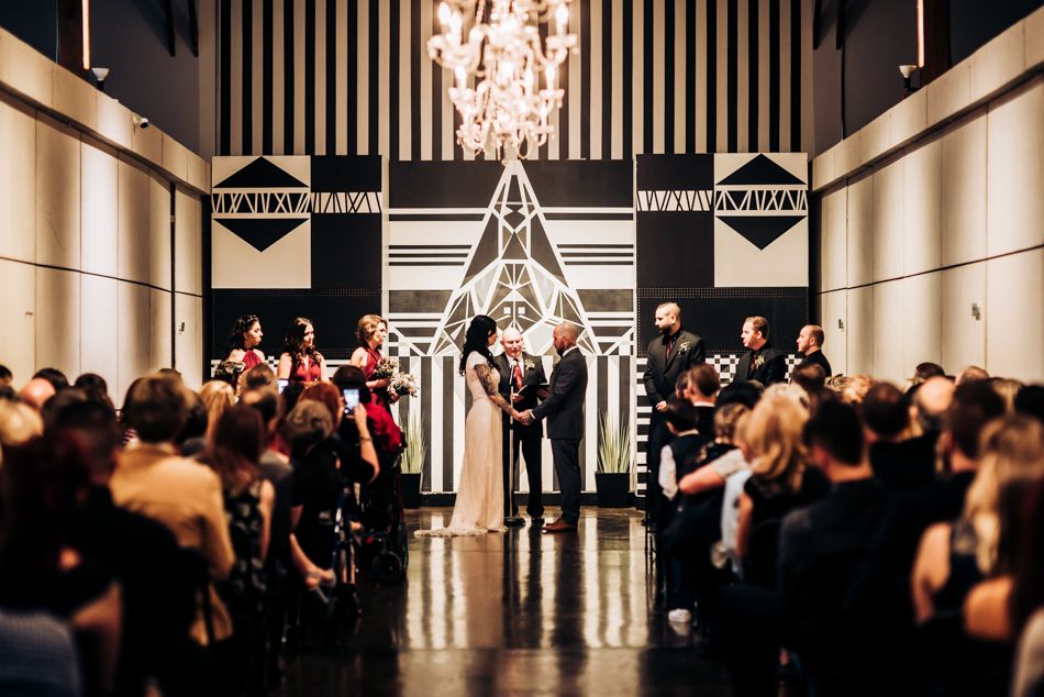 Wedding ceremony in a modern venue with art deco black and white geometric backdrop and chandeliers.
