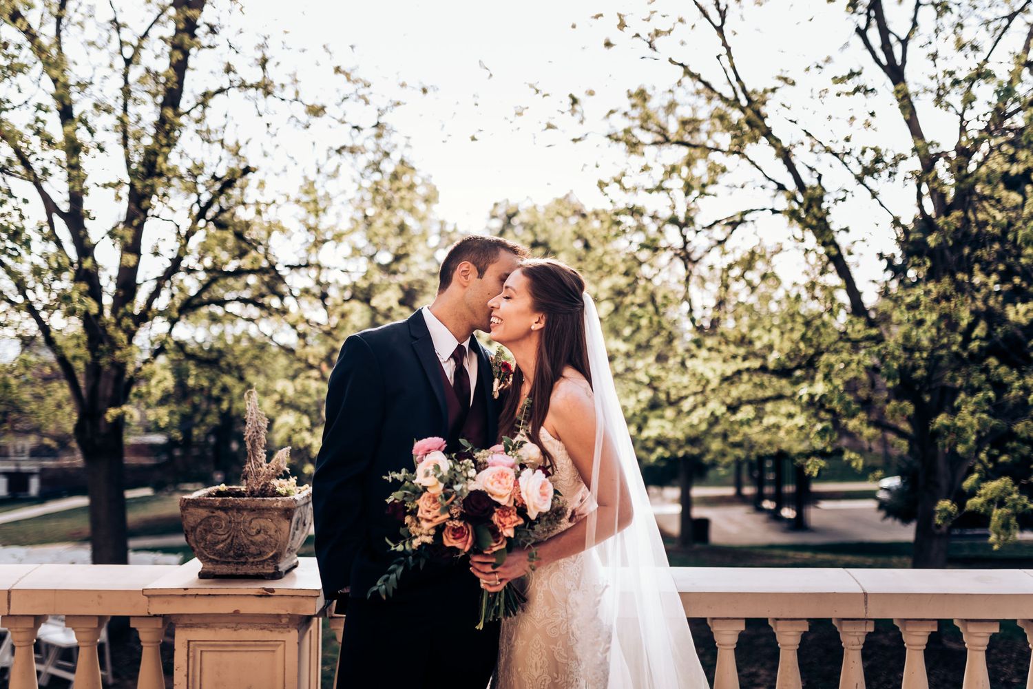 Couple sharing romantic moment on outdoor terrace with blooming trees in background.