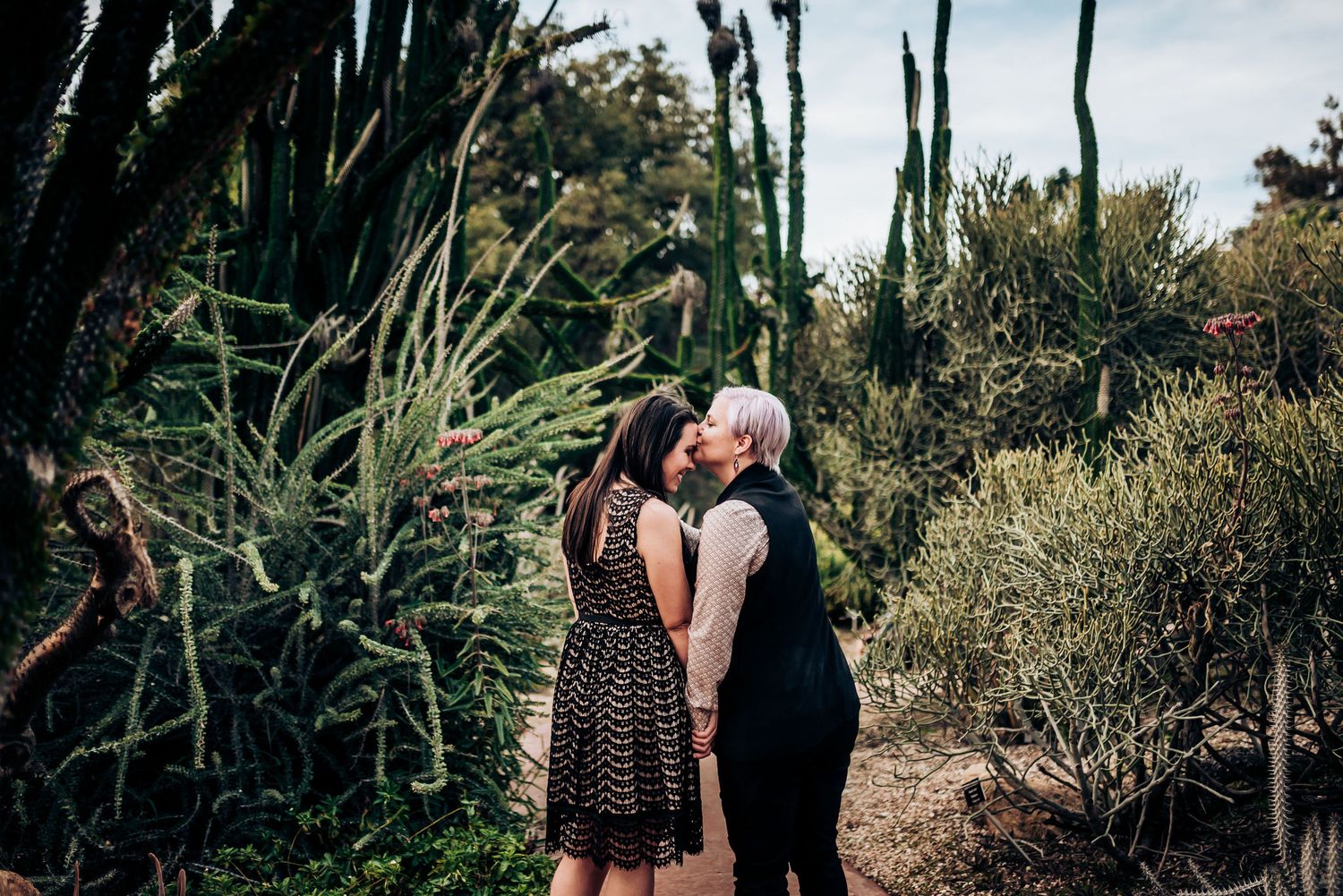 A tender moment shared between two people on a path surrounded by tall desert plants.