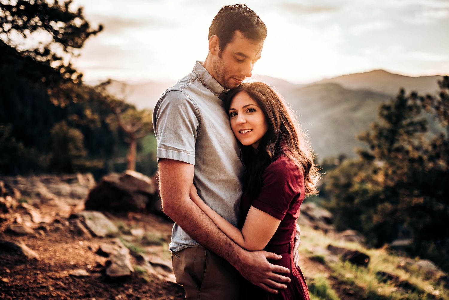 Couple in casual attire embracing on mountain trail with scenic valley view.