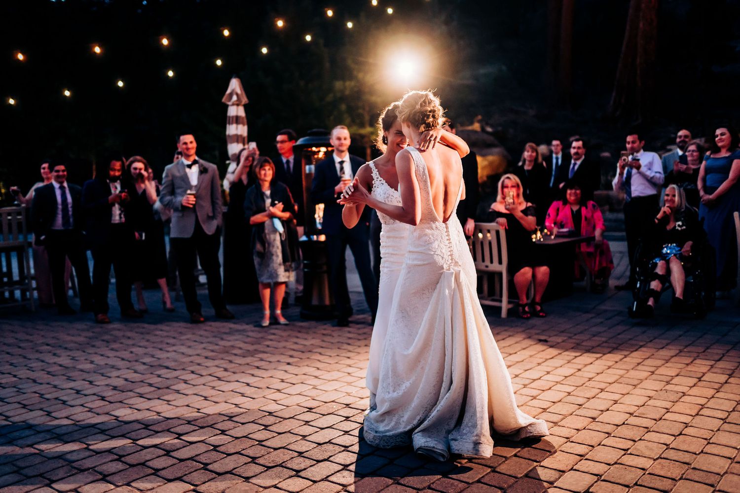 A romantic evening dance between two people in white wedding gowns under string lights.