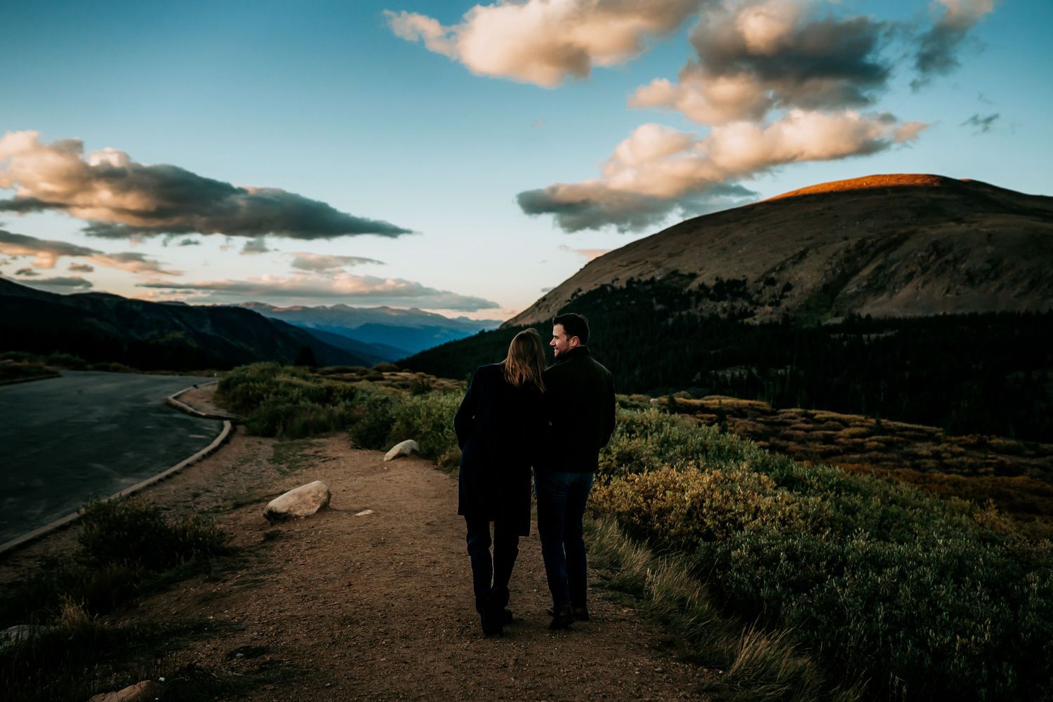 Scenic mountain landscape with winding road and dramatic clouds at sunset.