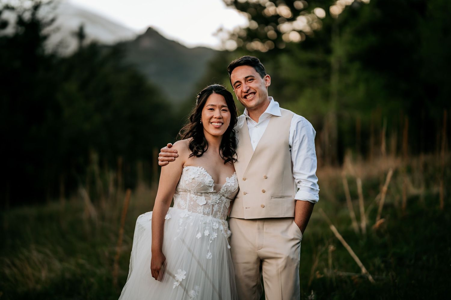 A couple shares a romantic moment in their wedding attire against a natural outdoor backdrop at sunset.