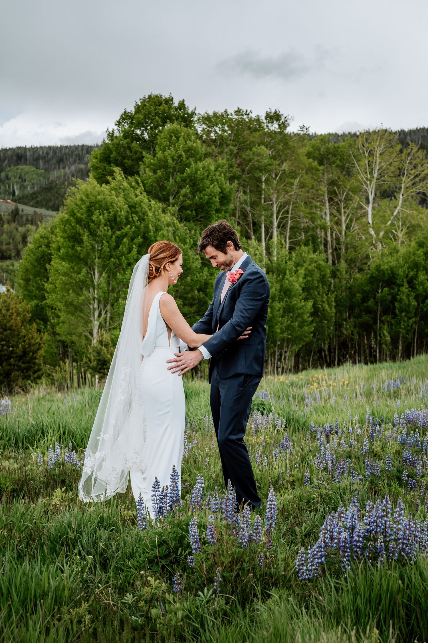 Newlyweds share an intimate moment in field of lupines with aspen grove backdrop.