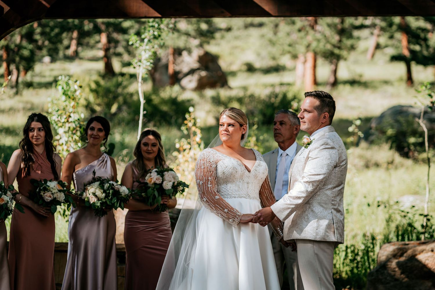 Outdoor wedding ceremony with wedding party standing under wooden arch.