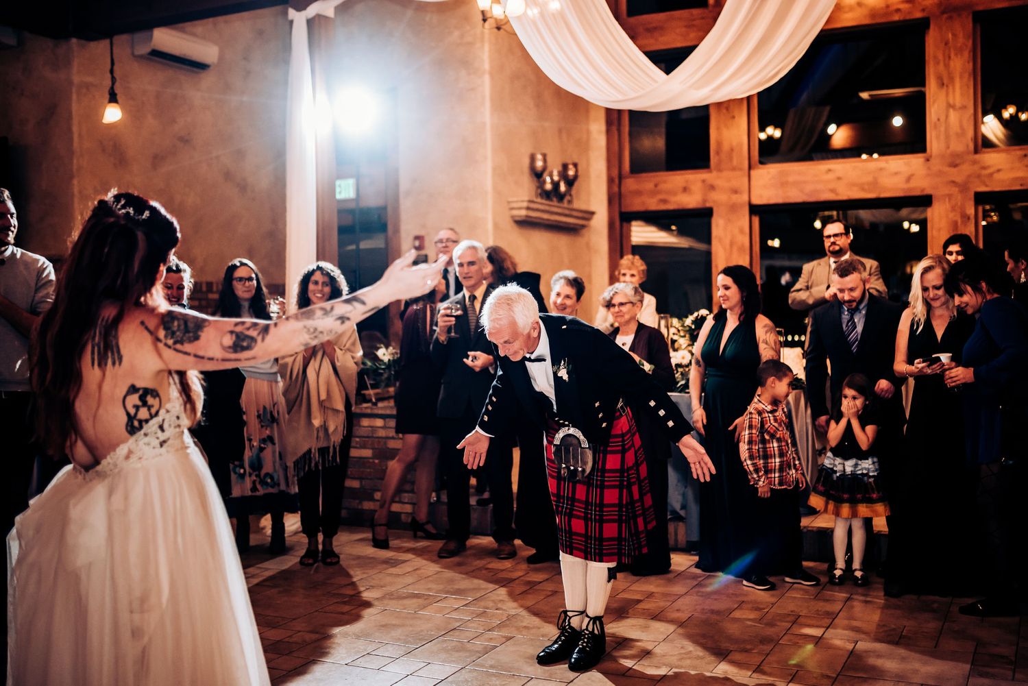 Bride dances with guest in kilt during Scottish wedding celebration.