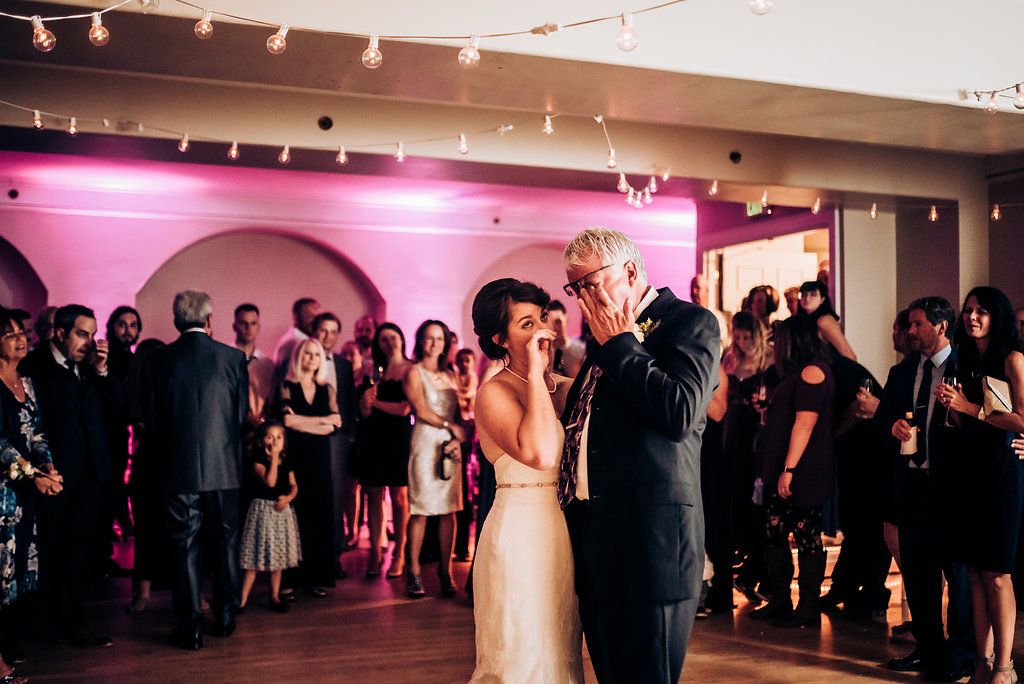 A couple shares an intimate slow dance during their wedding reception in a beautifully lit ballroom.