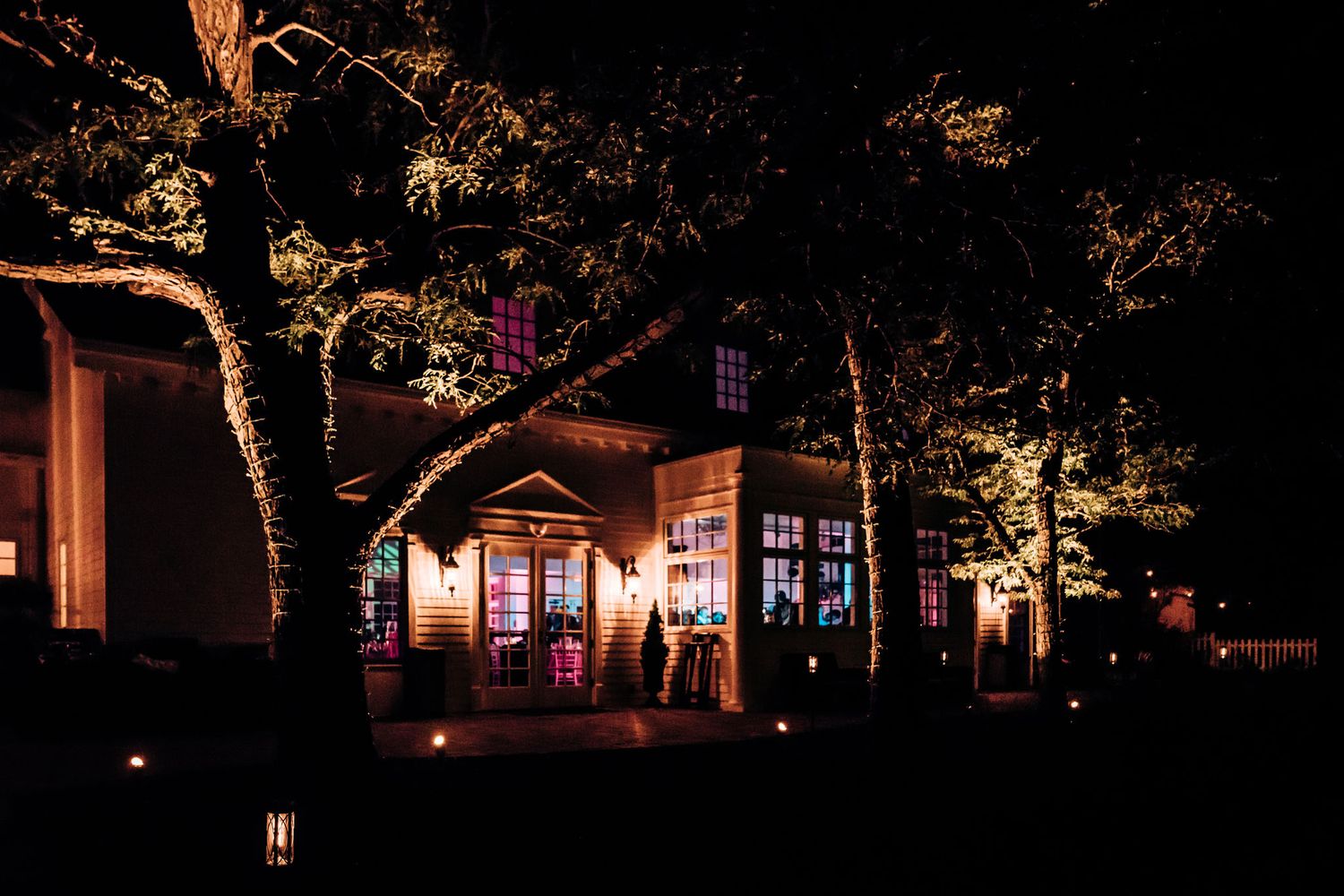 Wedding venue illuminated at night with pink lights glowing through windows and trees.