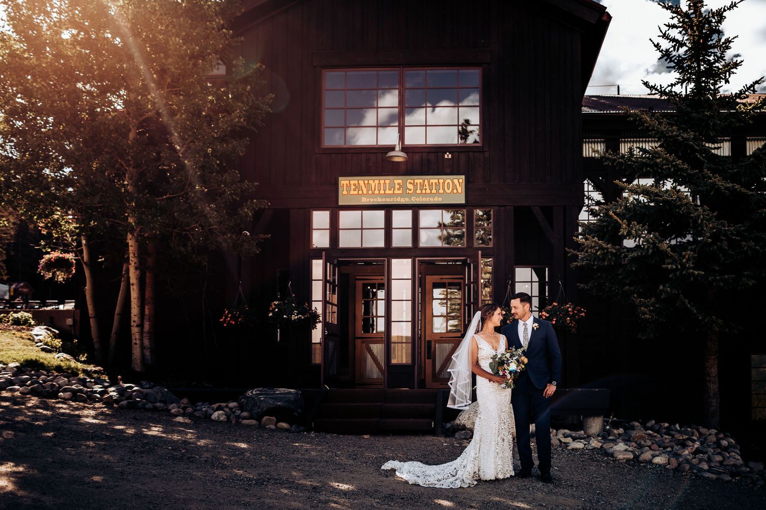 Wedding couple poses outside rustic mountain lodge at sunset.