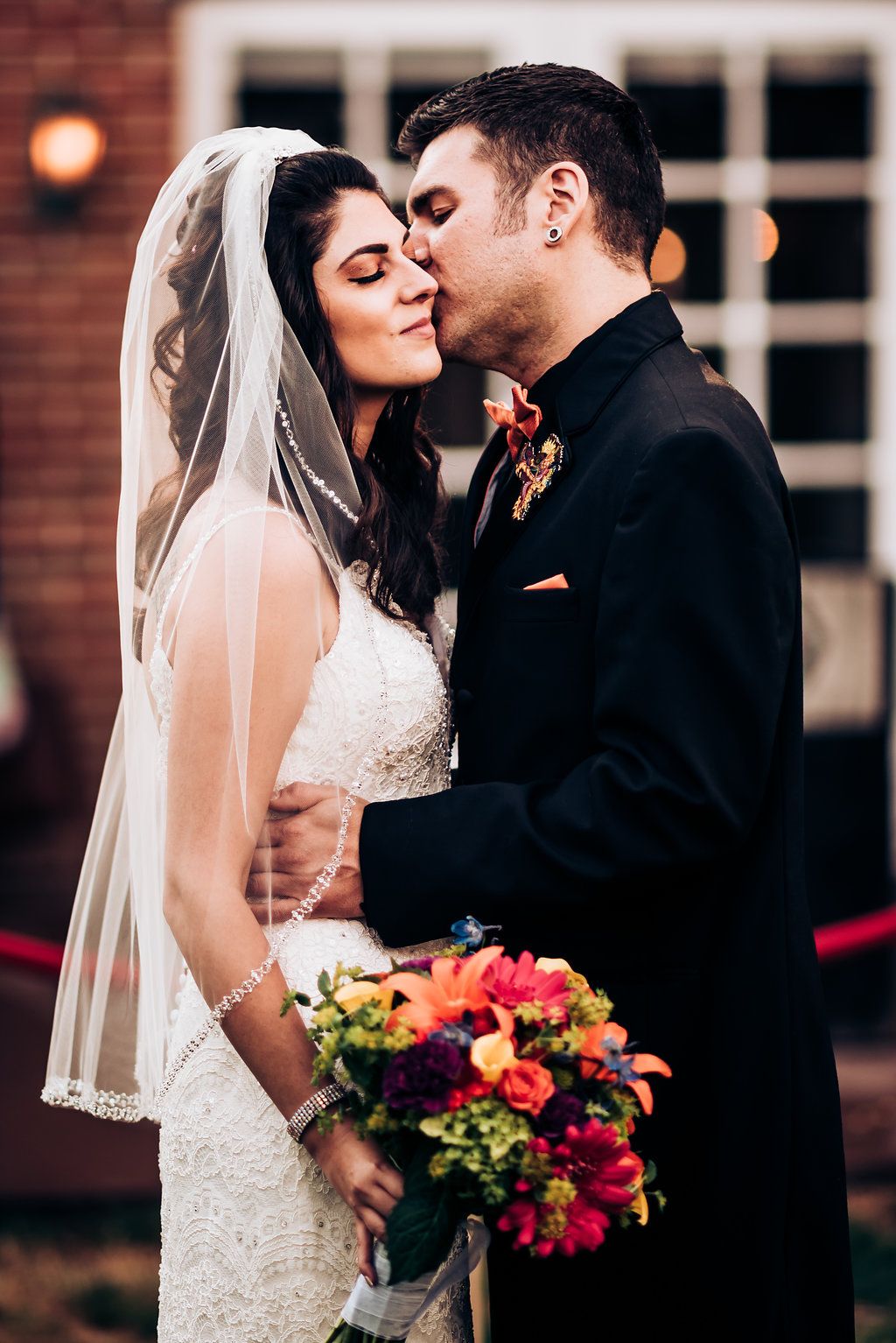 Intimate wedding moment outside a brick building with a colorful bouquet of flowers.