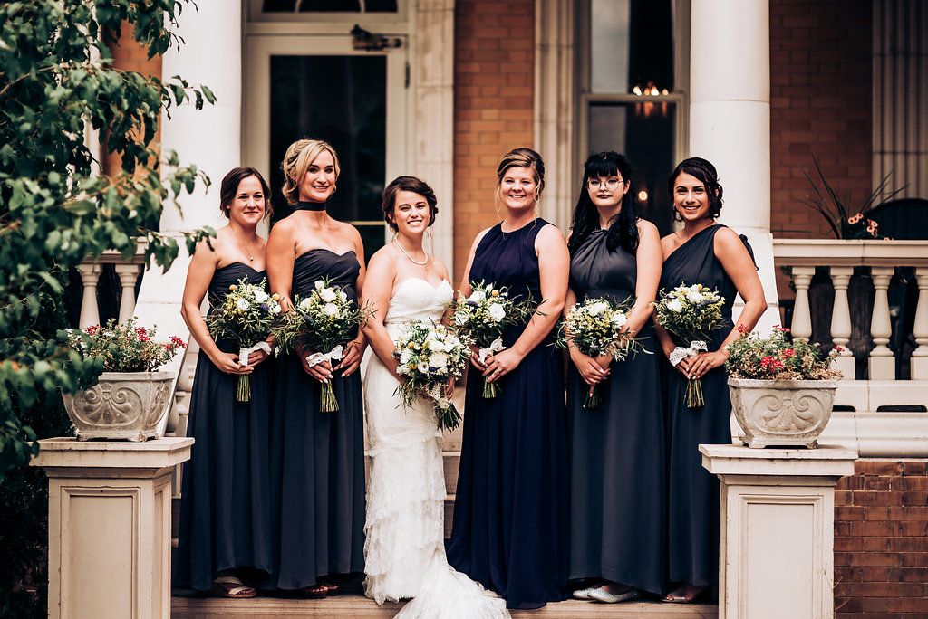 Bridal party in navy blue dresses poses on historic building steps with floral bouquets.