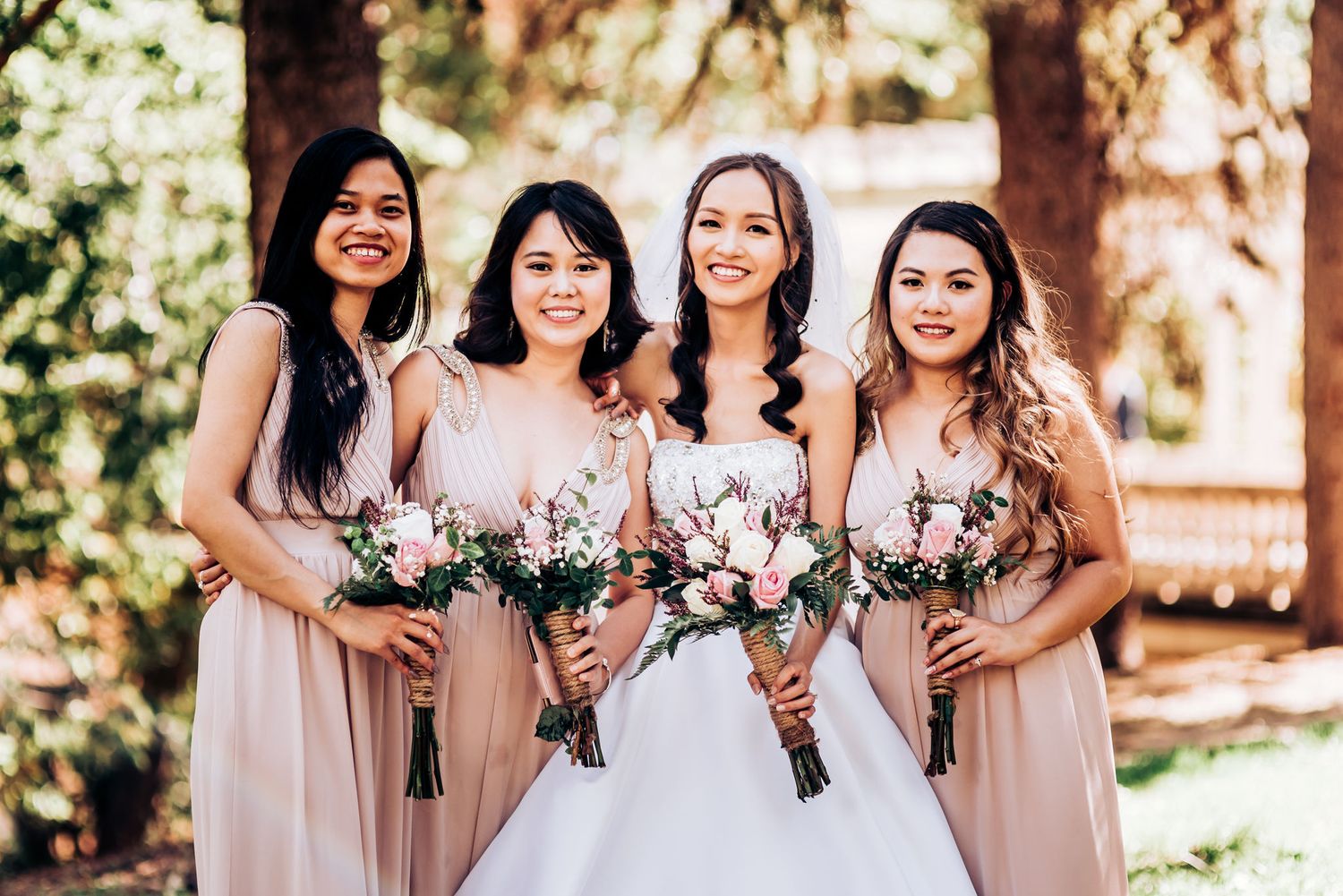 A bridal party of four poses with bouquets in blush pink dresses.