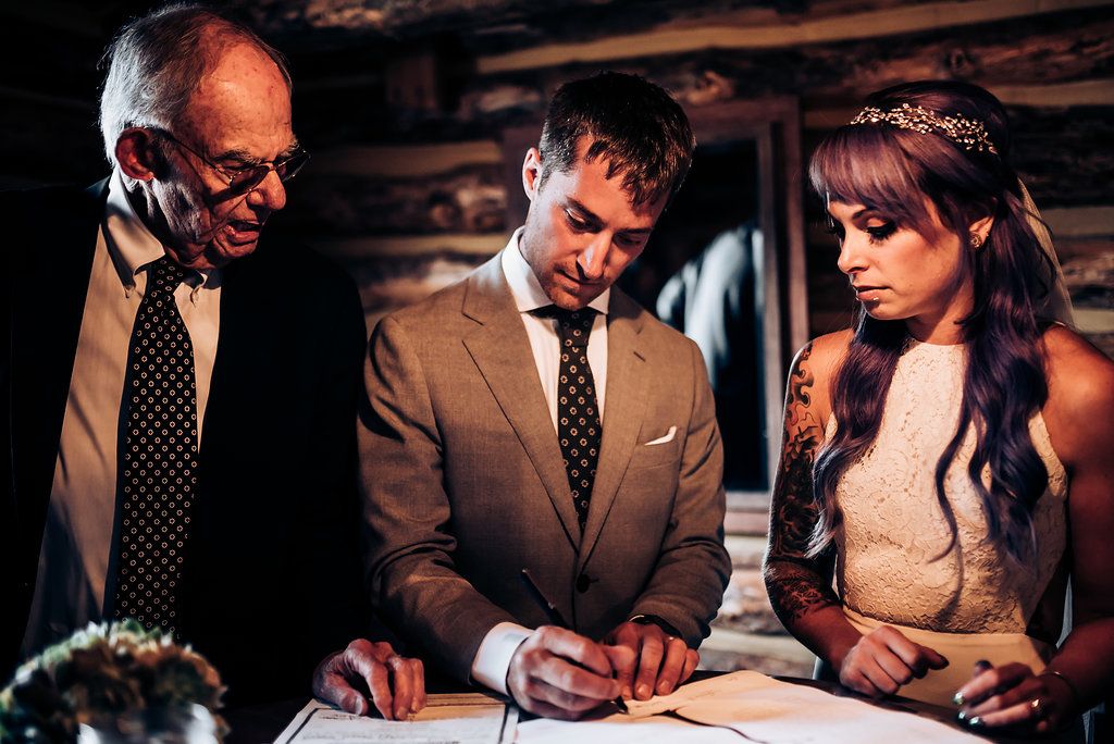 Three people reviewing and signing formal documents inside a cozy log cabin setting.