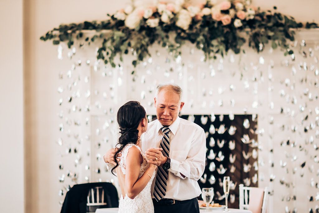 A touching dance moment in front of a floral backdrop at an indoor wedding reception.