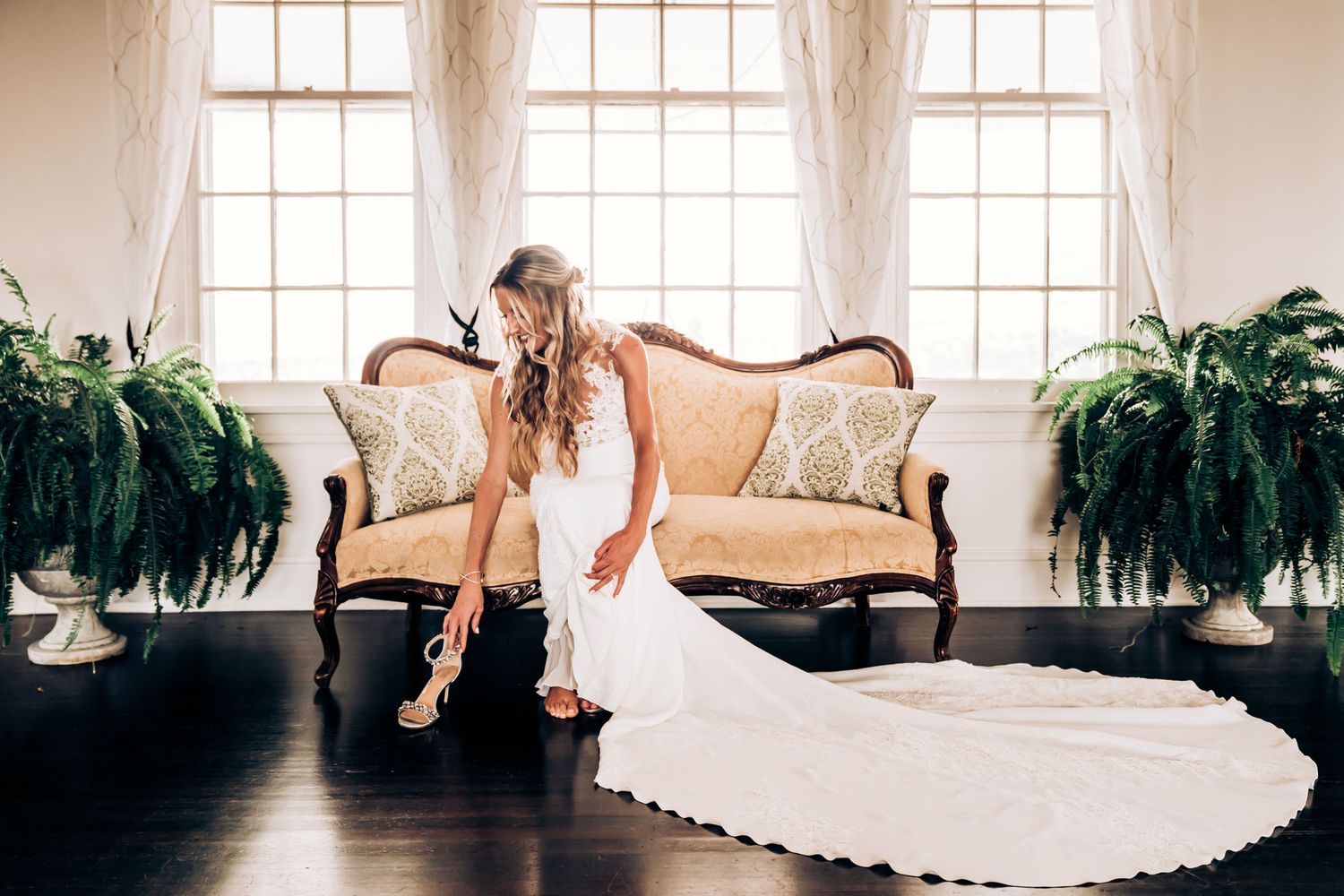Stunning bridal portrait on an antique sofa with trailing wedding dress and potted ferns.
