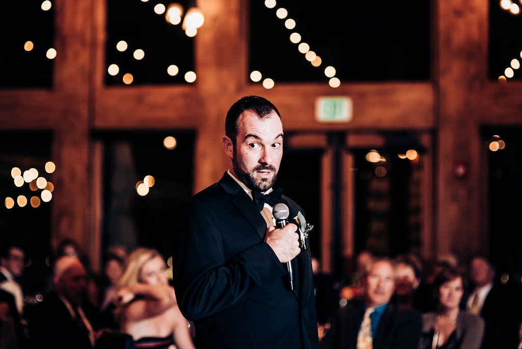 A speaker gives a heartfelt speech during a wedding reception under twinkling lights.