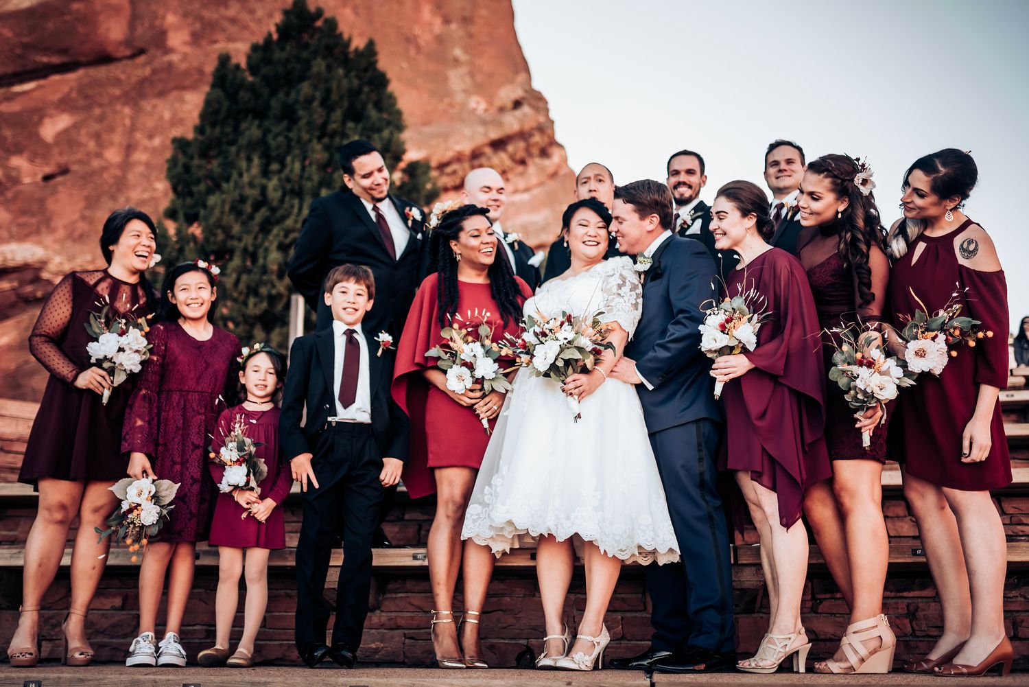 Wedding party in burgundy dresses pose together at Red Rocks amphitheater.