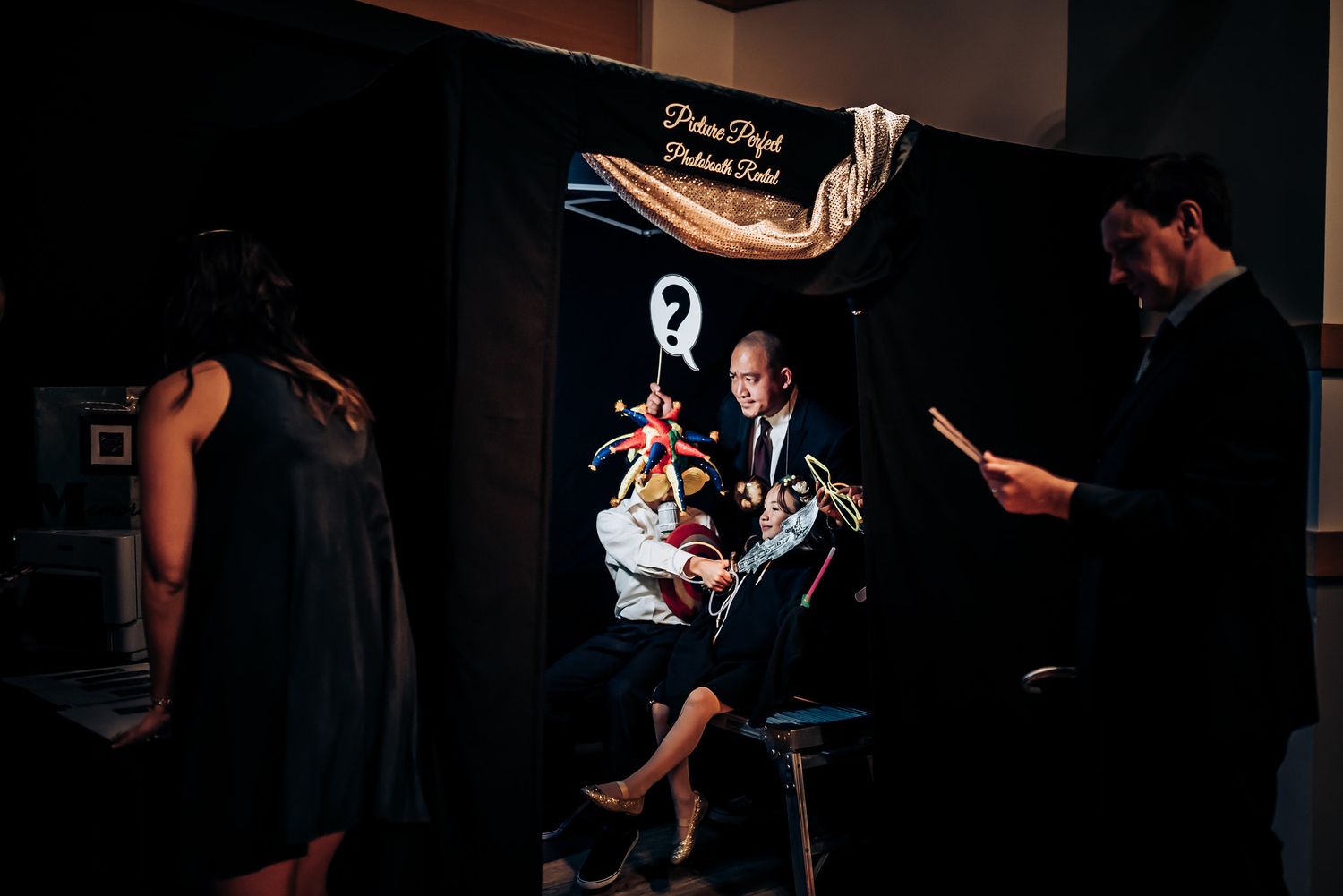 A dimly lit performance space with people gathered around a performer sitting on a stool.