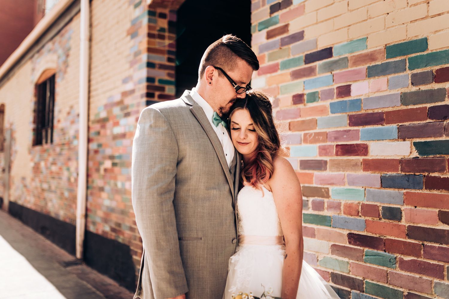 A tender wedding moment against a textured brick wall background.