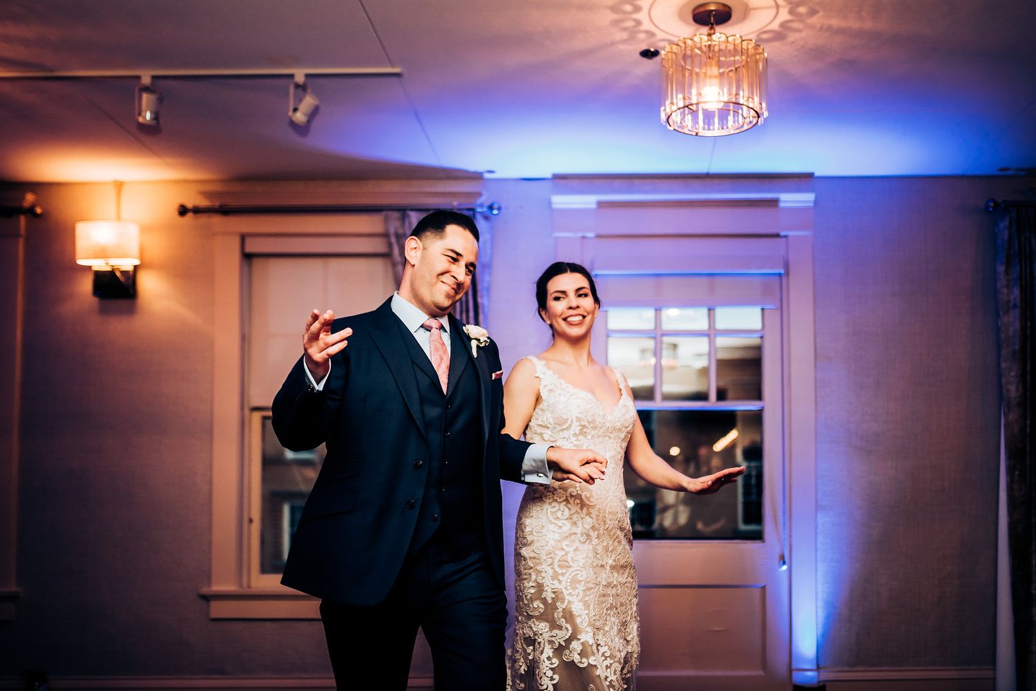 Couple dancing in reception room with blue uplighting and chandelier.