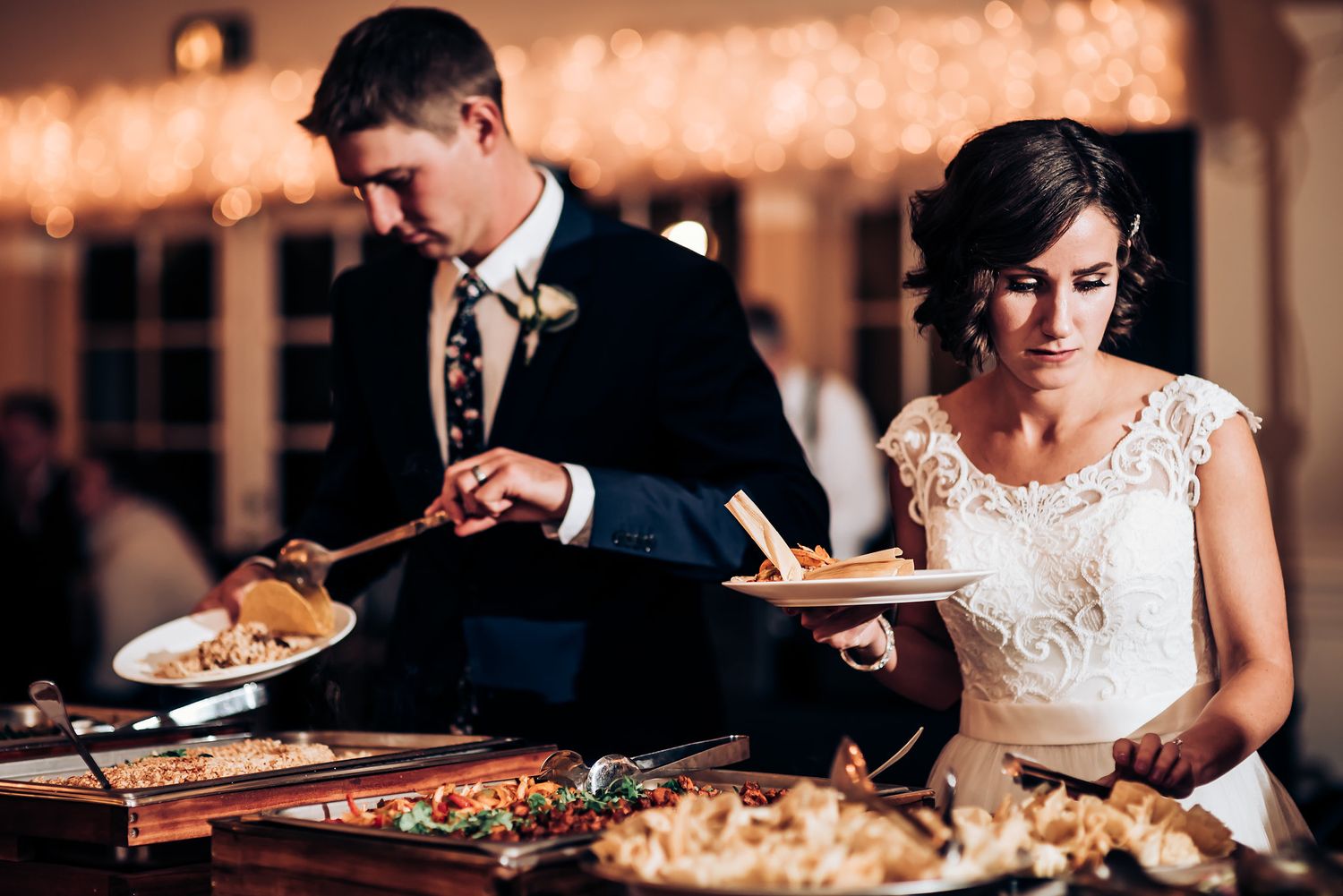 Couple serving food at their wedding reception buffet table.